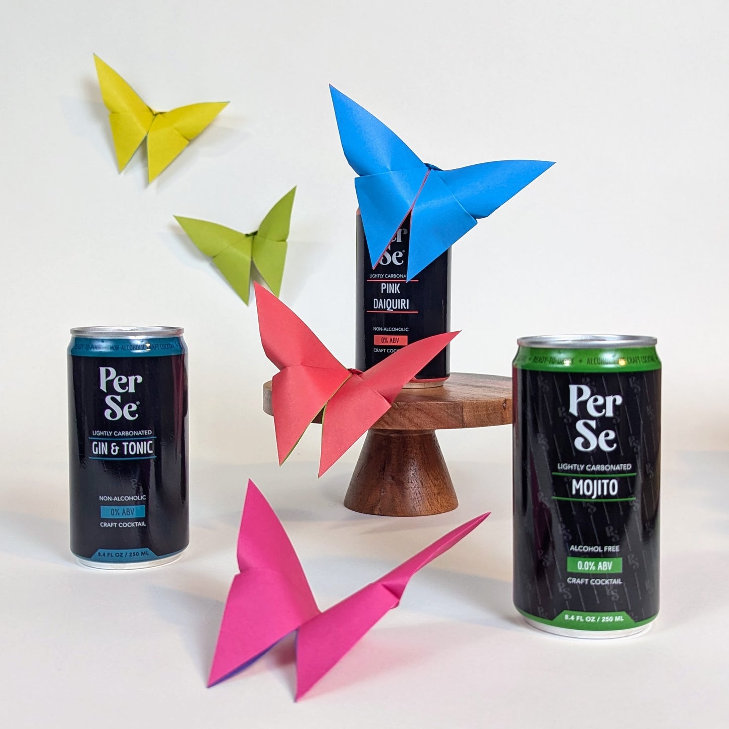 Per Se cocktail cans with colorful paper butterflies on a white background