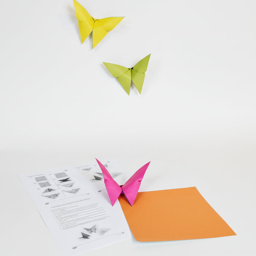 Three origami butterflies with instructions and a piece of orange origami paper.
